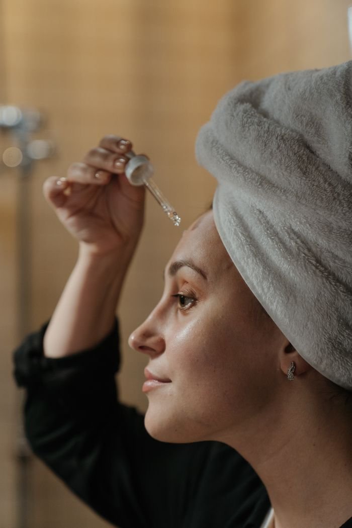 Home Close-up side view of a woman applying skincare serum with a dropper, promoting beauty routine.