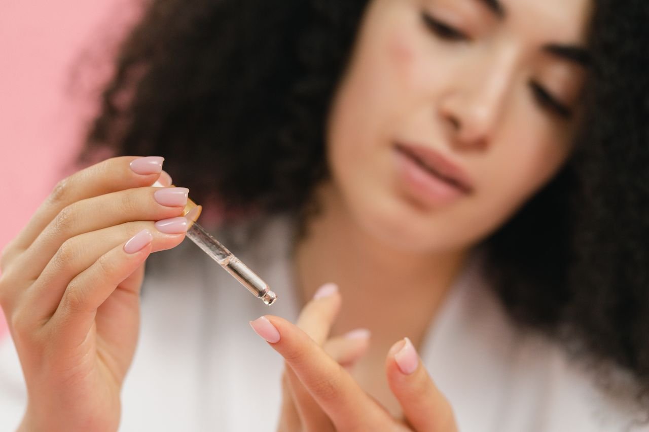 Home Close-up of a young woman applying skincare serum with a pipette against a pink background.